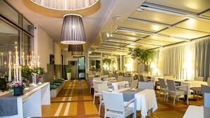 A restaurant with multiple tables and chairs, a tiled floor, and hanging pendant lights. - Hotel Santiago (Jesolo)