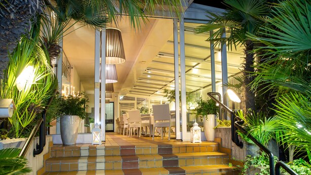A staircase with a checkered tile pattern leading to a seating area with chairs and tables, surrounded by potted plants and a railing. - Hotel Santiago (Jesolo)
