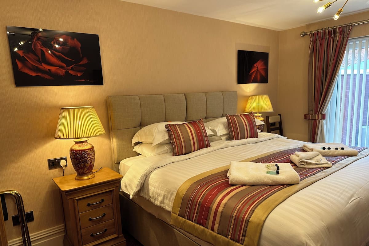 A hotel room with a bed, bedside lamps, a nightstand, a wooden dresser, and a painting on the wall.