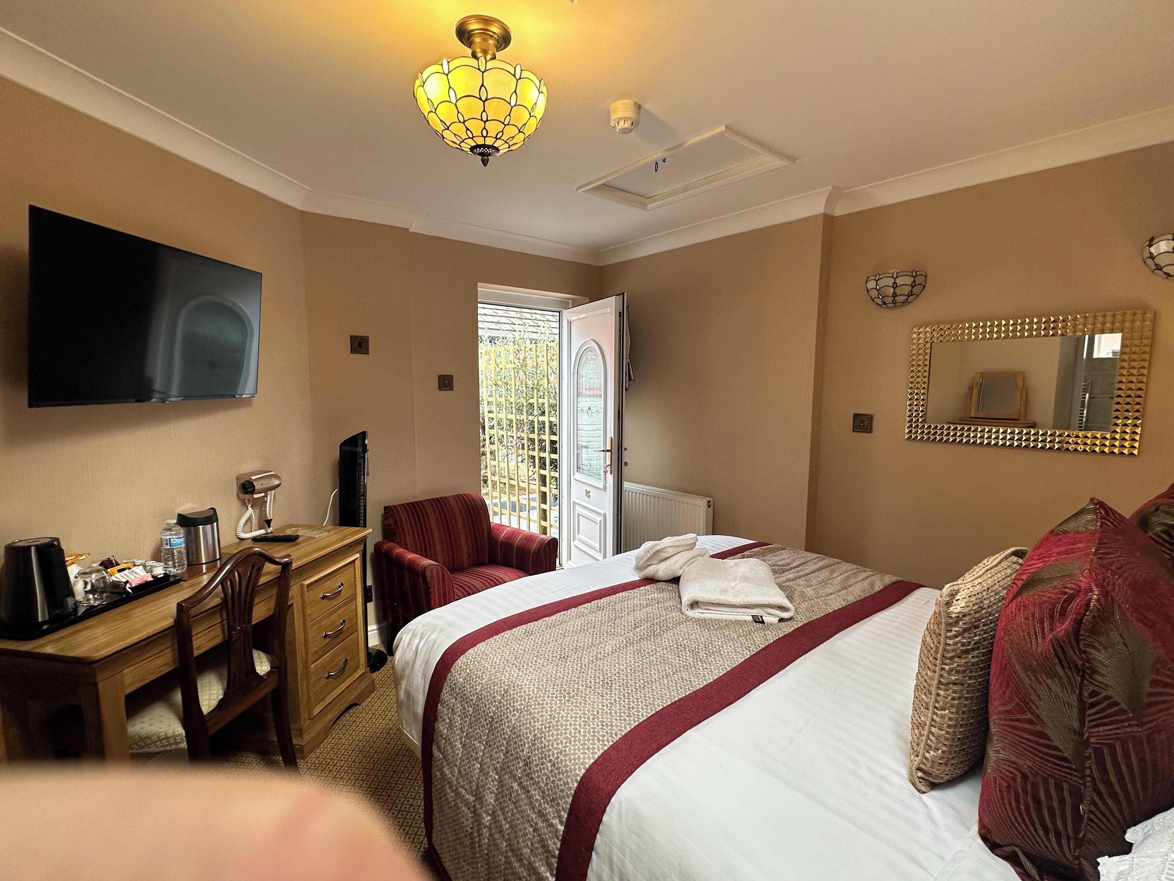 A hotel room with a bed, a desk with a computer, a chair, a television, and a window with a view of the outside.