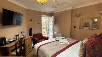 A hotel room with a bed, a desk with a computer, a chair, a television, and a window with a view of the outside.