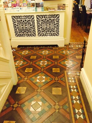 Um corredor com piso de azulejos estampados e uma área de recepção com um painel decorativo.