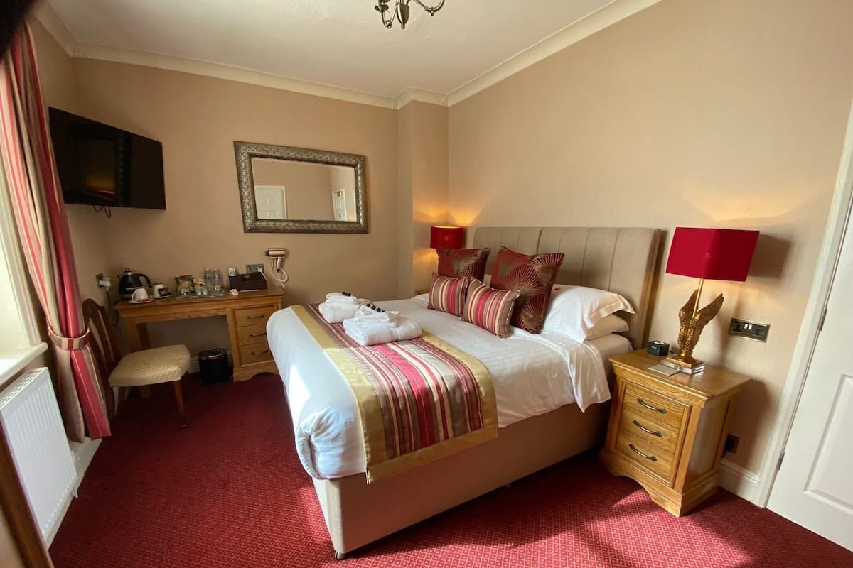 A hotel room with a bed, bedside tables, a desk, a chair, a mirror, and a television.