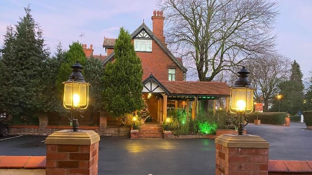 A traditional brick house with a well-lit entrance, a covered porch, and a driveway leading to the front door. - Chester House Guest House (Chester)