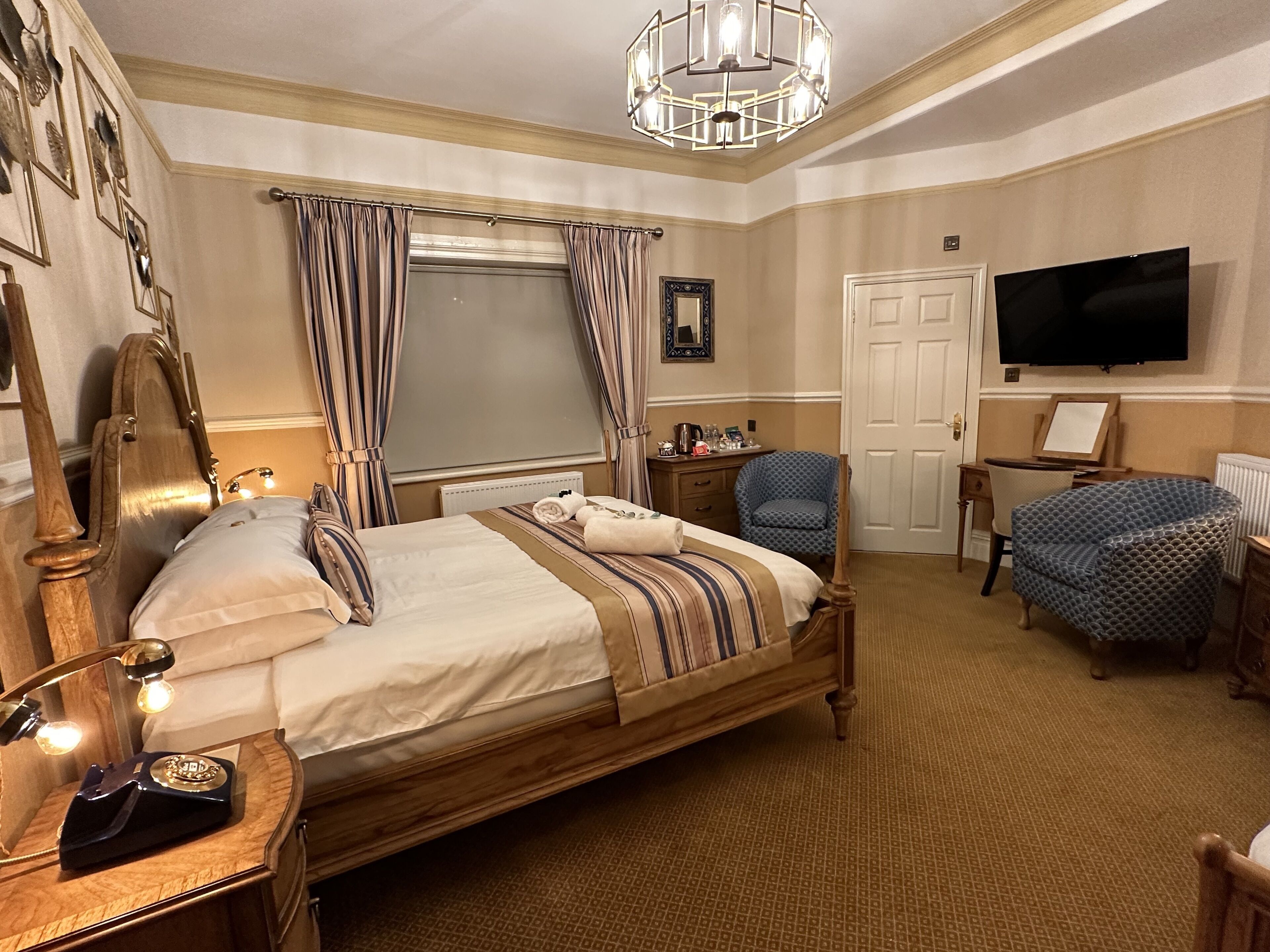 Ein Hotelzimmer mit einem hölzernen Bett, einem Schreibtisch mit Stuhl, einem Fernseher und einem großen Fenster mit Vorhängen.