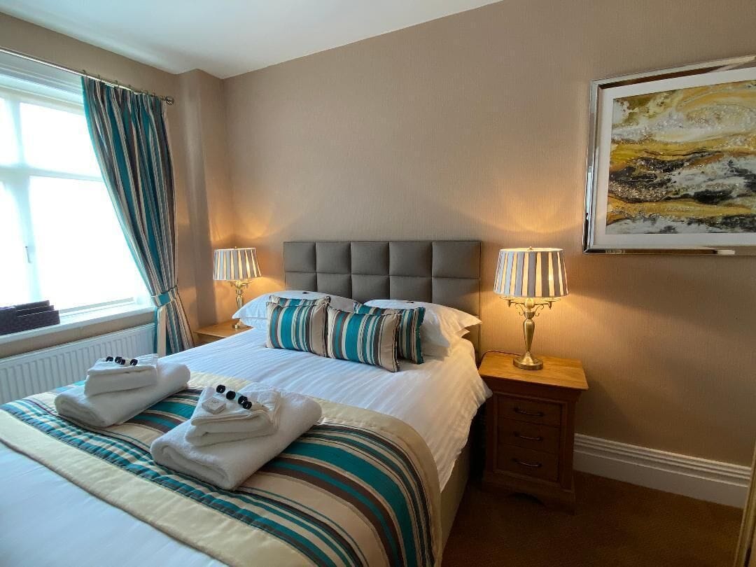 A hotel room with a large bed, two bedside lamps, a framed artwork on the wall, and a window with curtains.