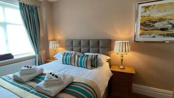 A hotel room with a large bed, two bedside lamps, a framed artwork on the wall, and a window with curtains.