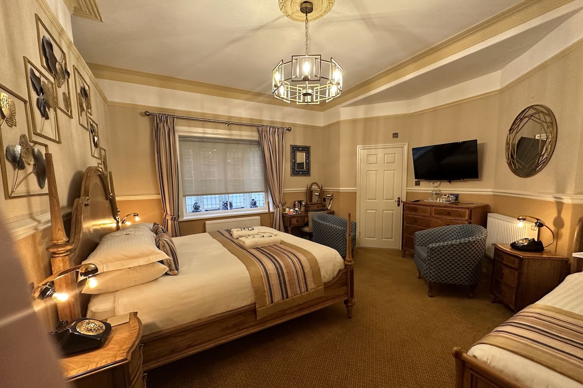 A hotel room with a large bed, a desk, a chair, a television, and a window with curtains.