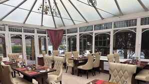 A conservatory with multiple tables and chairs, large windows, and a chandelier. - Chester House Guest House (Chester)