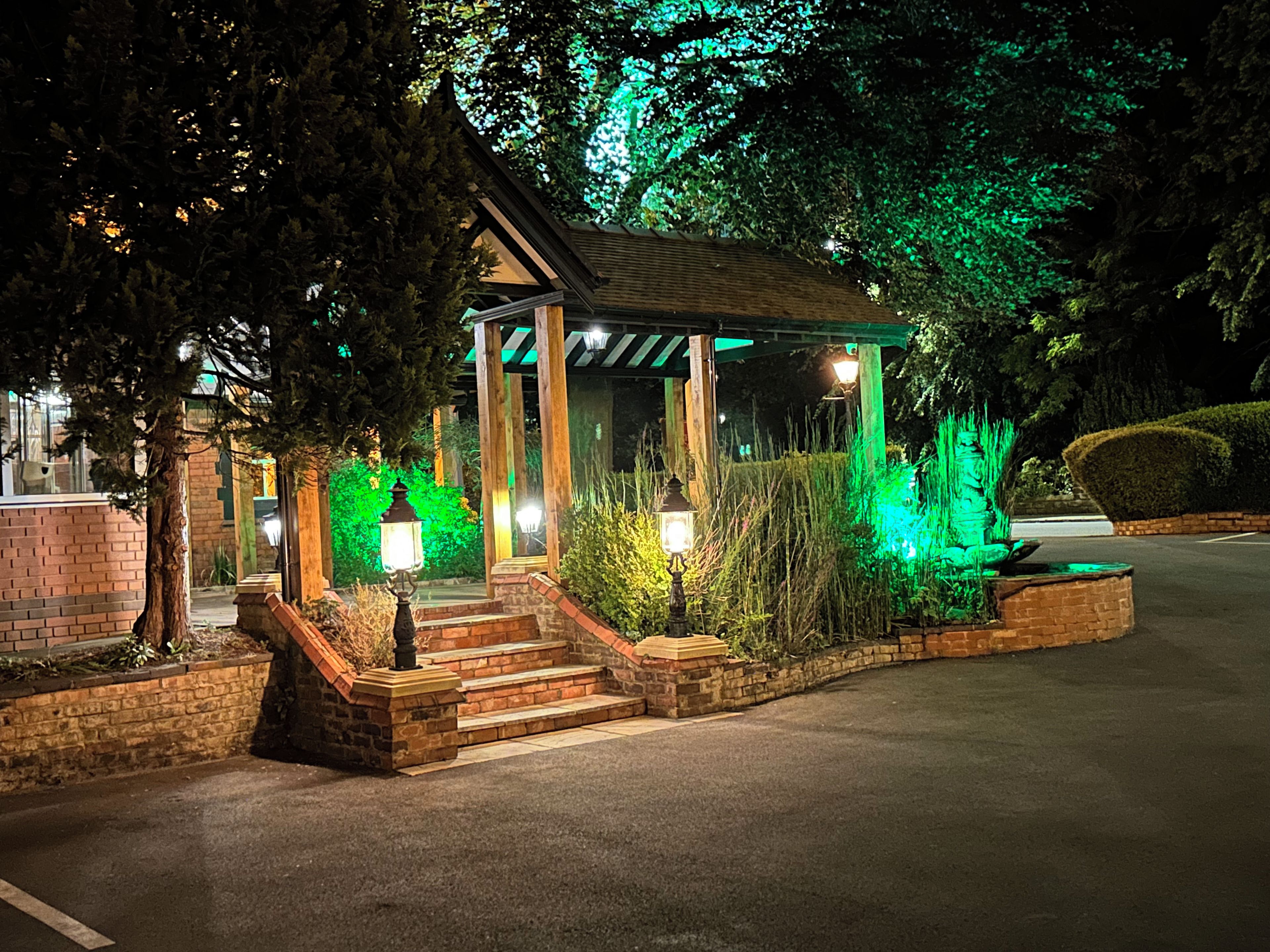 Um gazebo com degraus que o levam, rodeado por vegetação e iluminado por luzes.