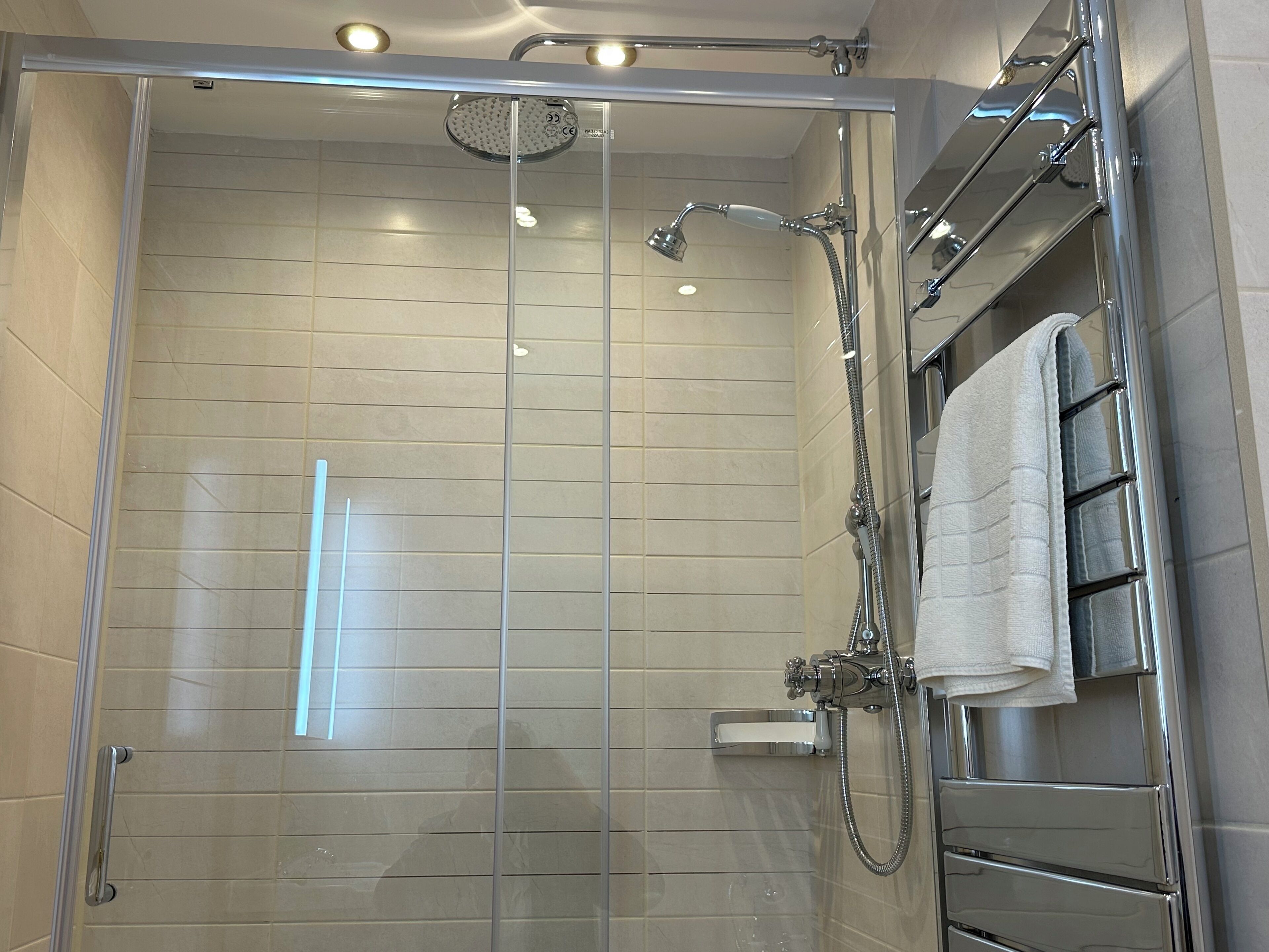 A modern shower with a glass door, chrome fixtures, and a towel rack.