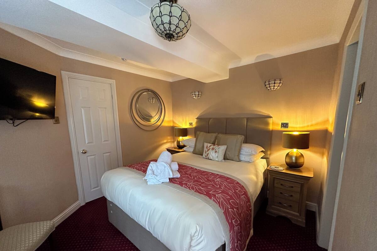 A hotel room with a large bed, bedside lamps, a round mirror, and a flat-screen TV mounted on the wall.