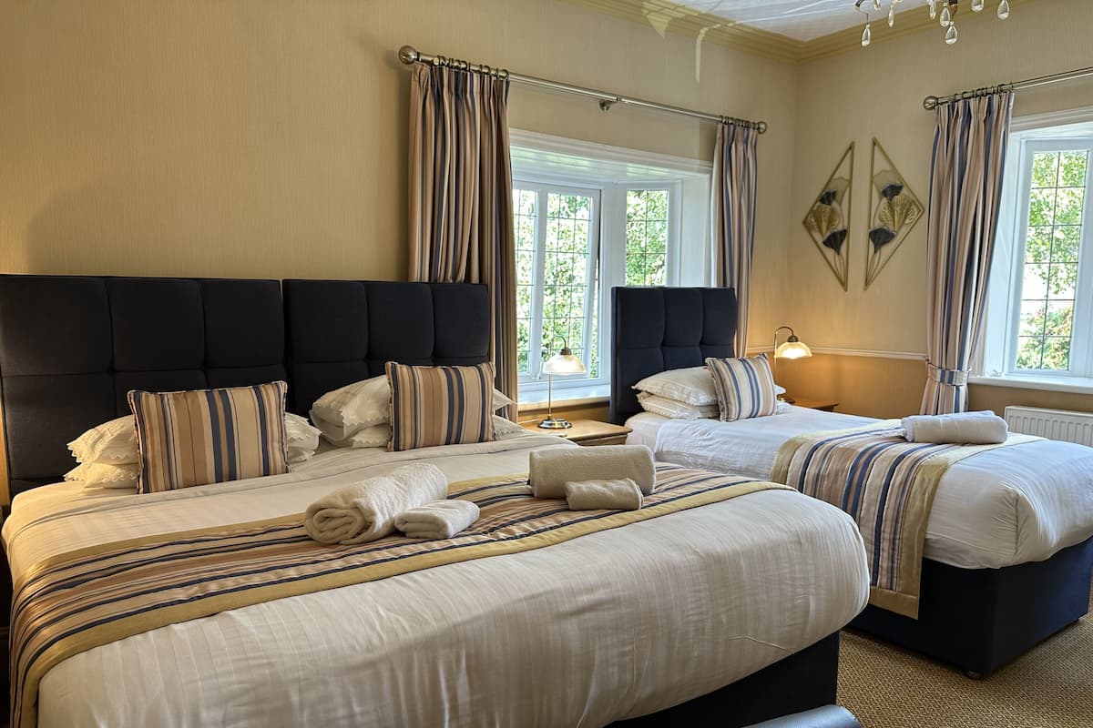 A hotel room with two beds, a large headboard, and a view of greenery outside.