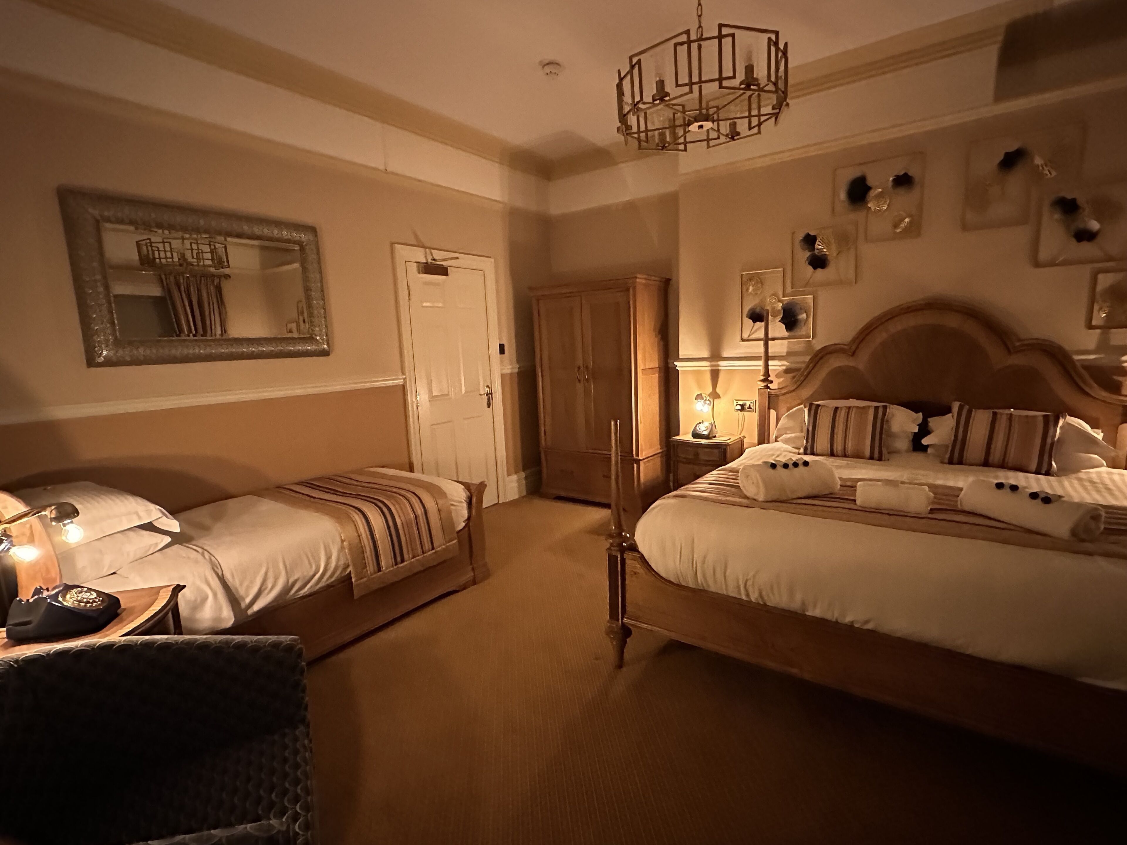 Une chambre d’hôtel avec deux lits simples, un grand miroir, une armoire et un lustre.