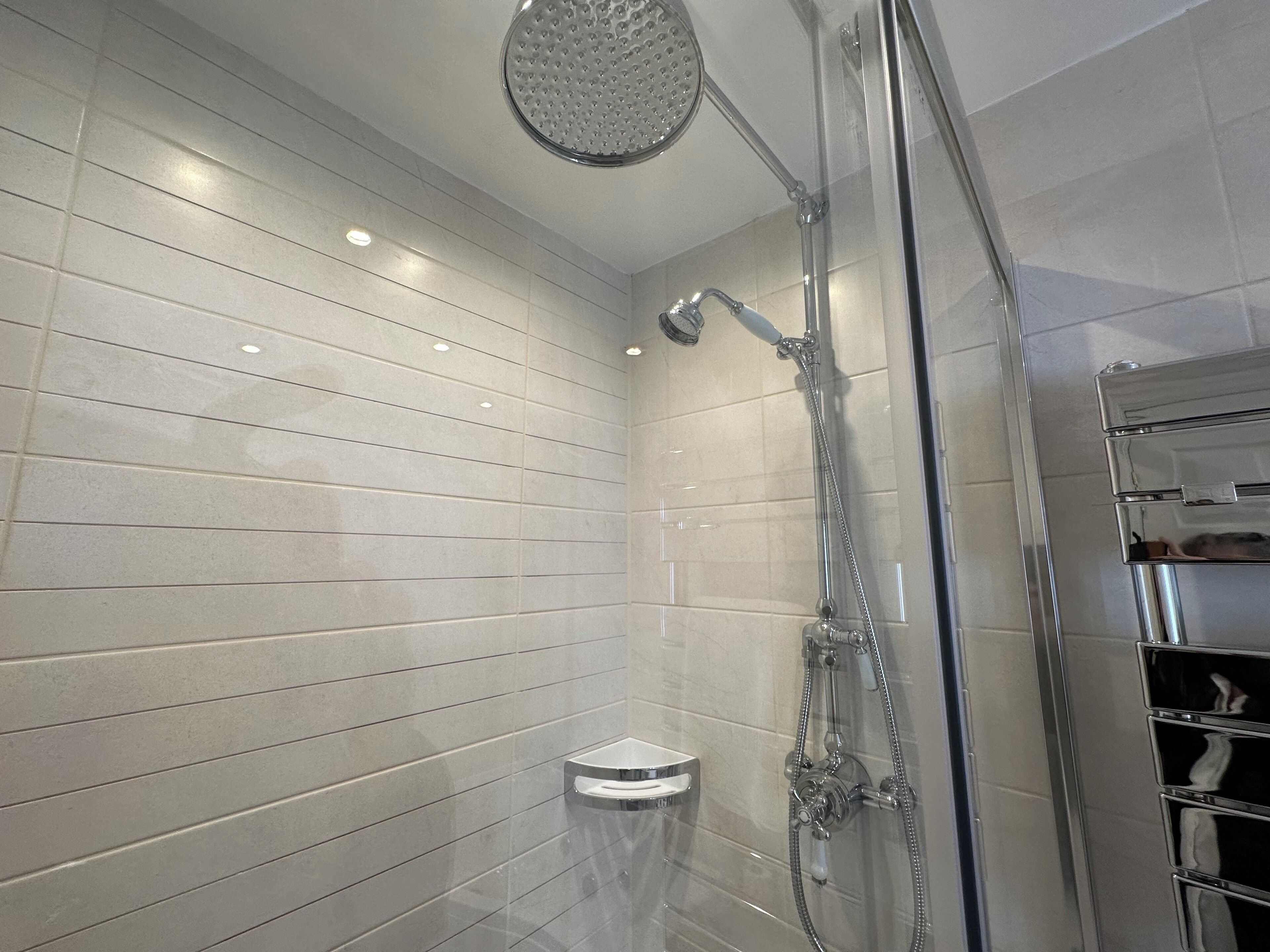 A modern shower with a glass enclosure, a handheld showerhead, and a wall-mounted faucet.