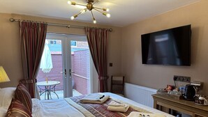 A hotel room with a bed, a TV, a desk with a coffee maker, and a view of the outside. - Chester House Guest House (Chester)