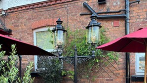 An outdoor patio with brick walls, two ornate street lamps, and red umbrellas. - Chester House Guest House (Chester)