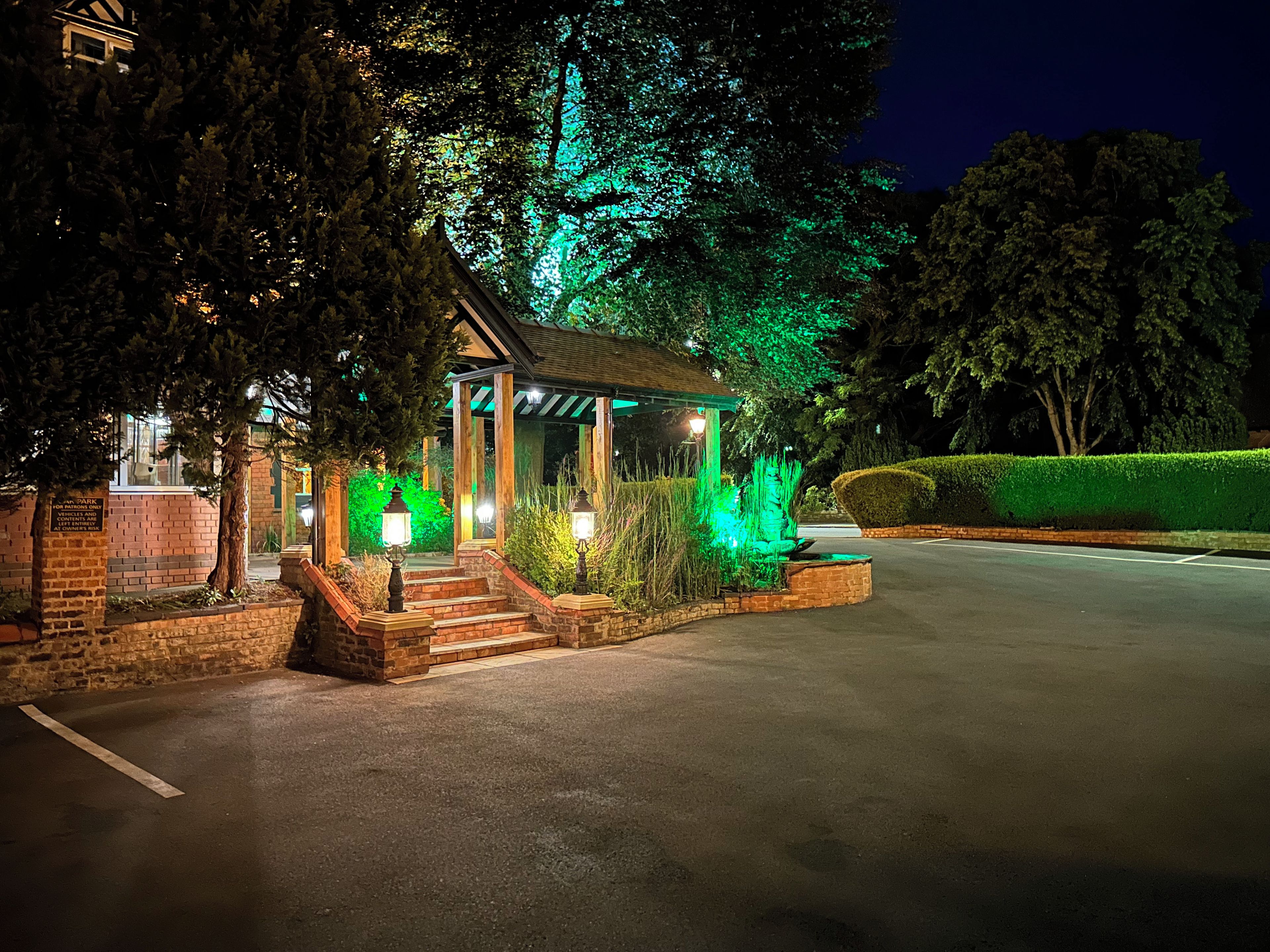 A gazebo with steps leading up to it, surrounded by greenery and a brick wall.