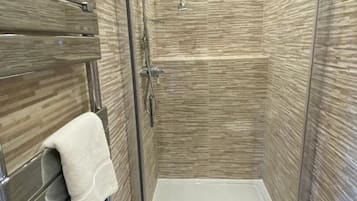 Une cabine de douche moderne dotée d’une porte en verre, d’un pommeau de douche blanc et d’un porte-serviettes avec une serviette blanche.