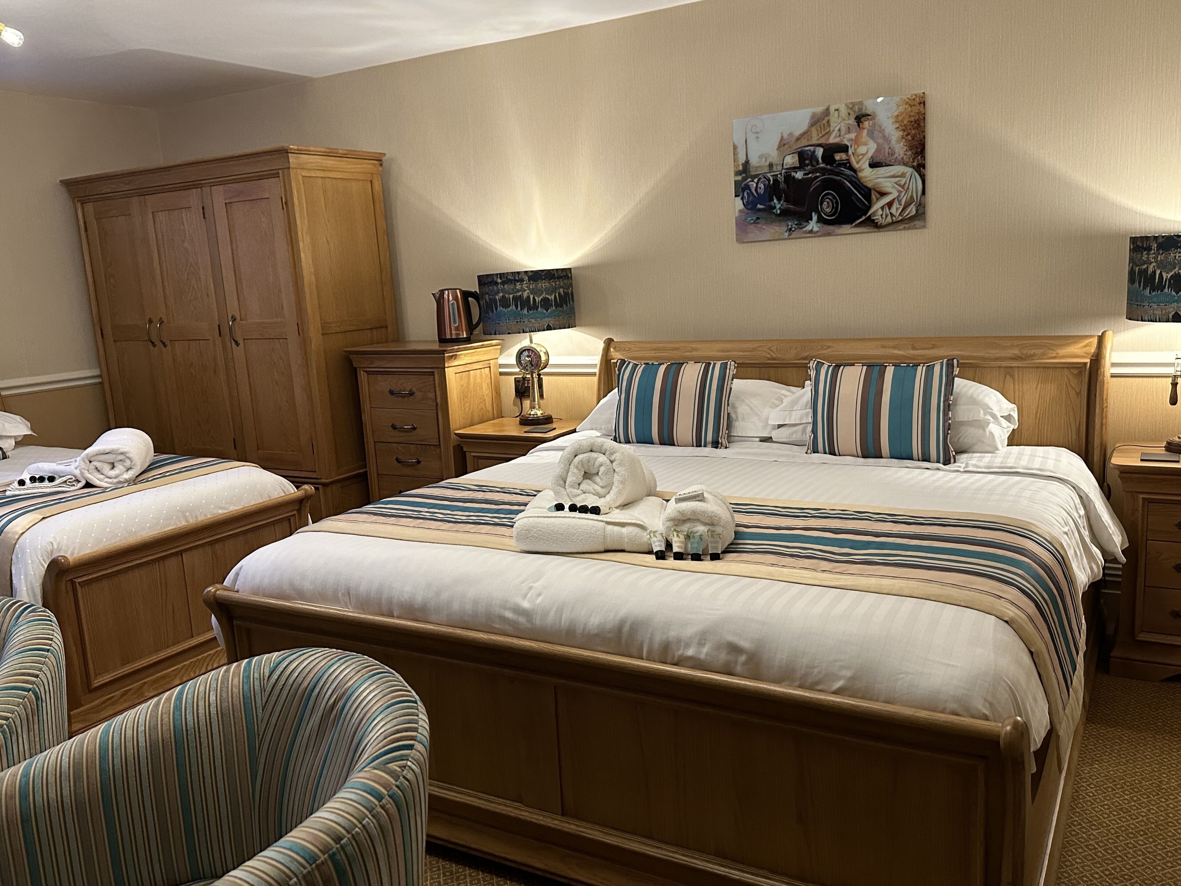 A hotel room with a large bed, two bedside tables, a wooden wardrobe, and a painting on the wall.