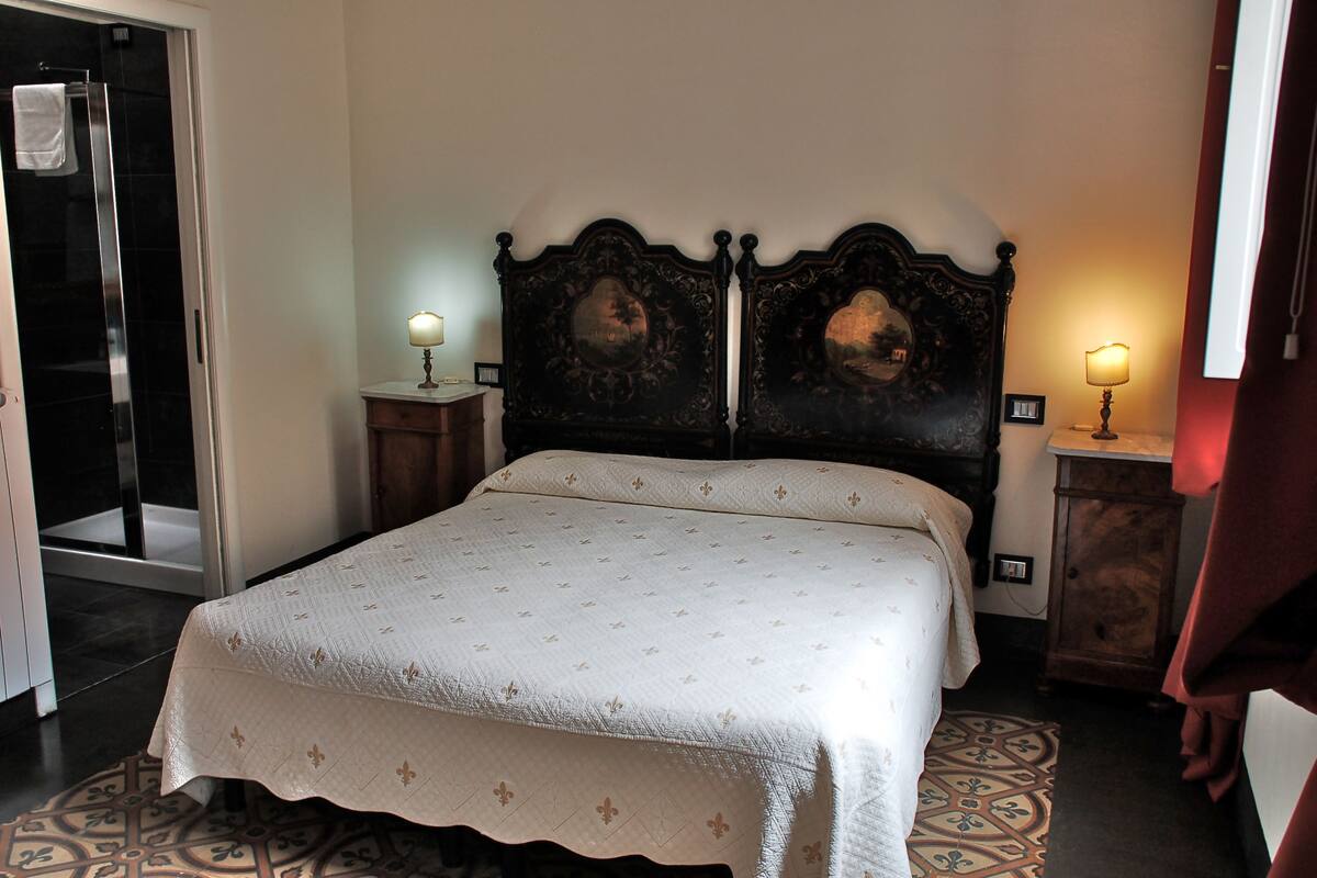 Un letto rifatto con cura, con una coperta a motivi, una testiera in legno scuro, due lampade ai comodini e un tappeto decorato sul pavimento.