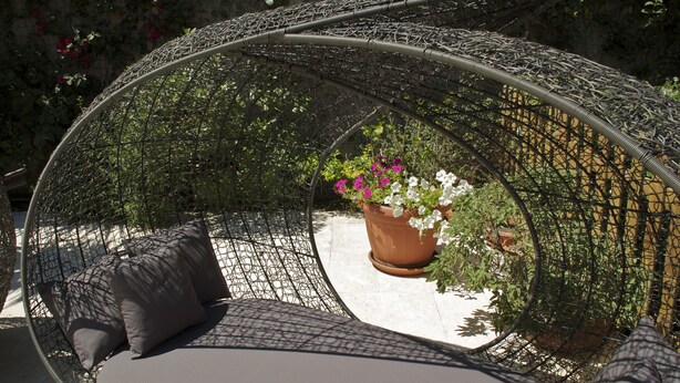 Een rond buitenzitgedeelte met geweven stoelen, kussens en een potplant.