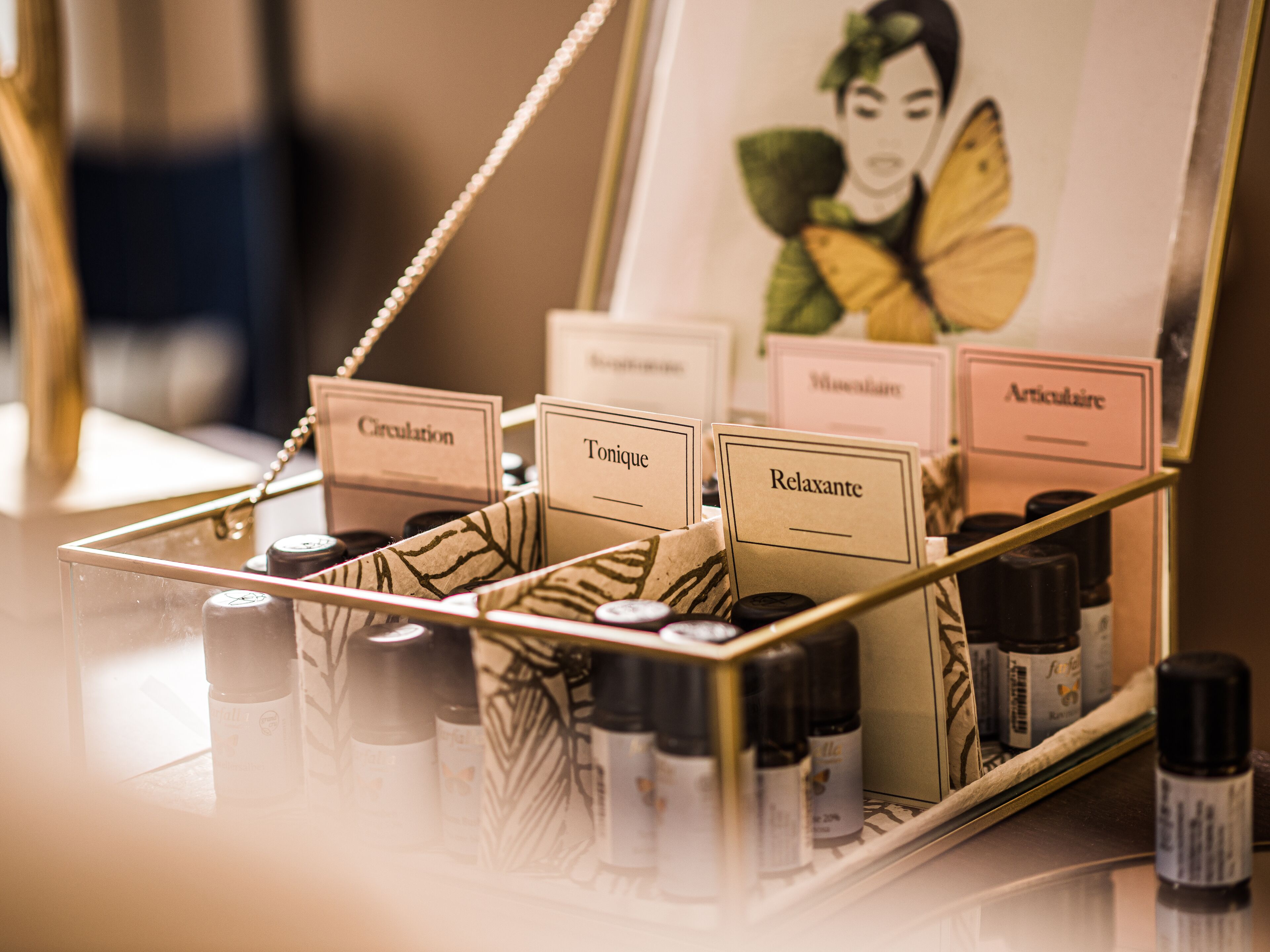 A display of essential oils in a glass container with labels for 'Circulation', 'Tonic', 'Relaxante', 'Mélanide', and 'Articulatrice'.