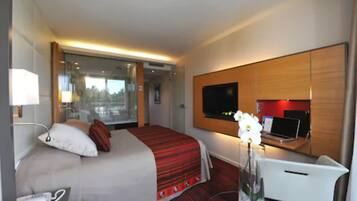 A hotel room with a bed, a desk with a laptop, a TV, and a vase with flowers.