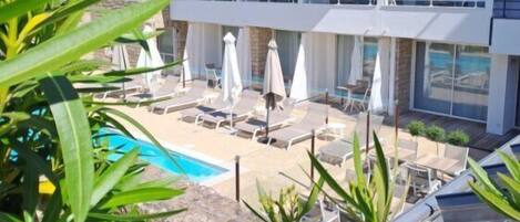 Un hotel de varios pisos con balcones, piscina y mobiliario exterior.