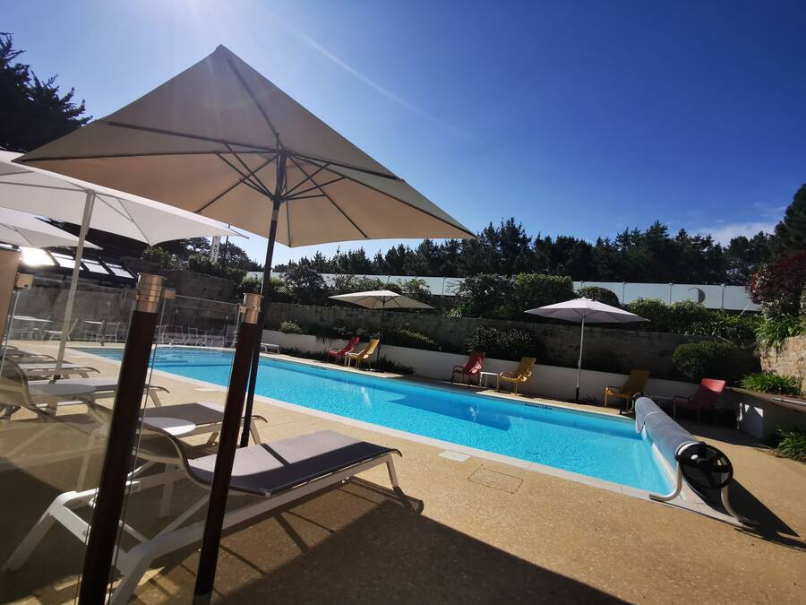 Piscina con sillones de descanso y sombrillas, rodeada por un muro de piedra y follaje.