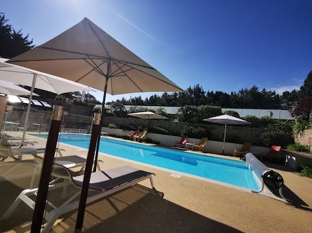 Una piscina al aire libre, sombrillas, sillones reclinables de piscina