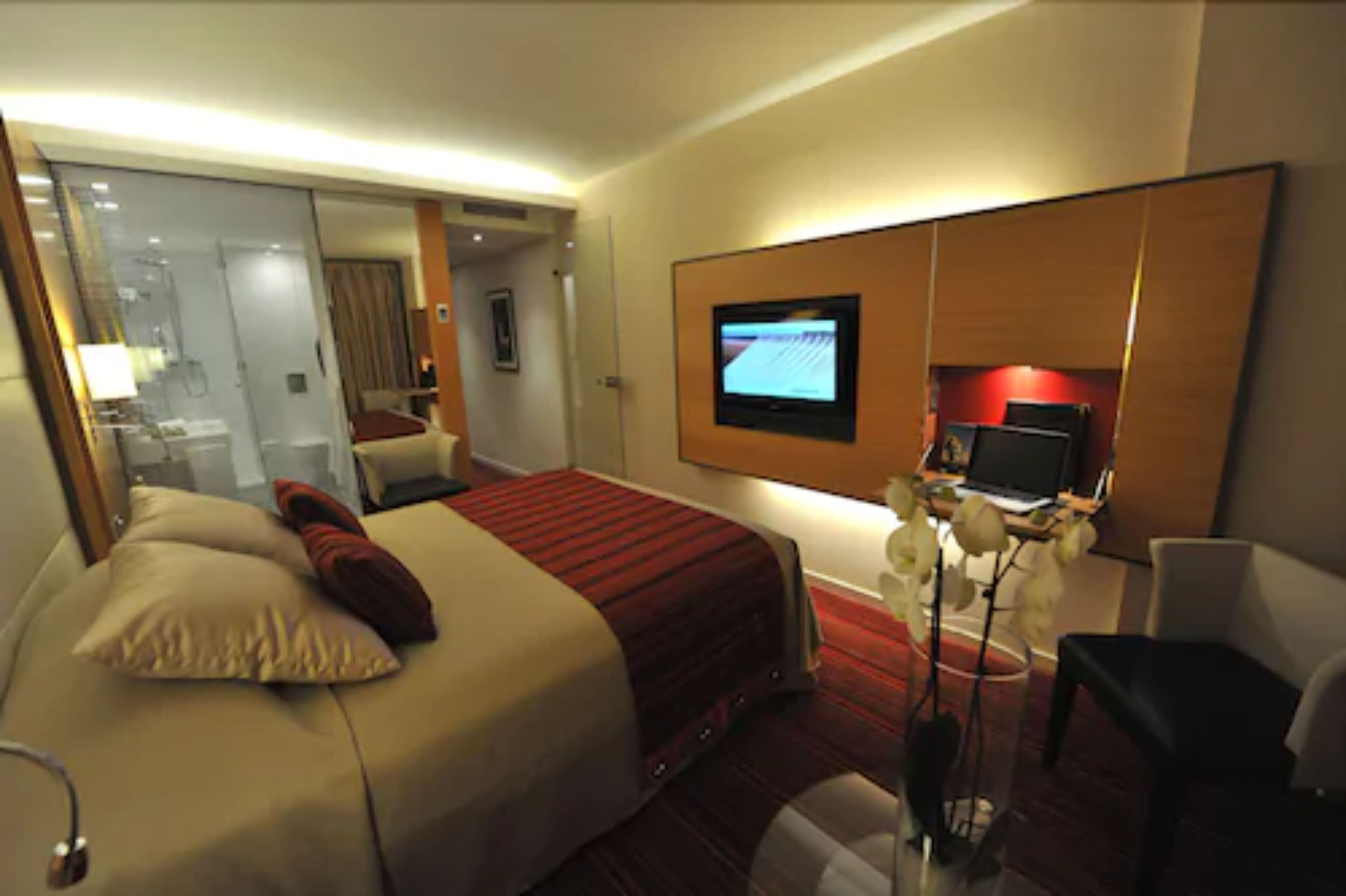 A hotel room with a large bed, a desk with a computer, a TV mounted on the wall, and a mirror.