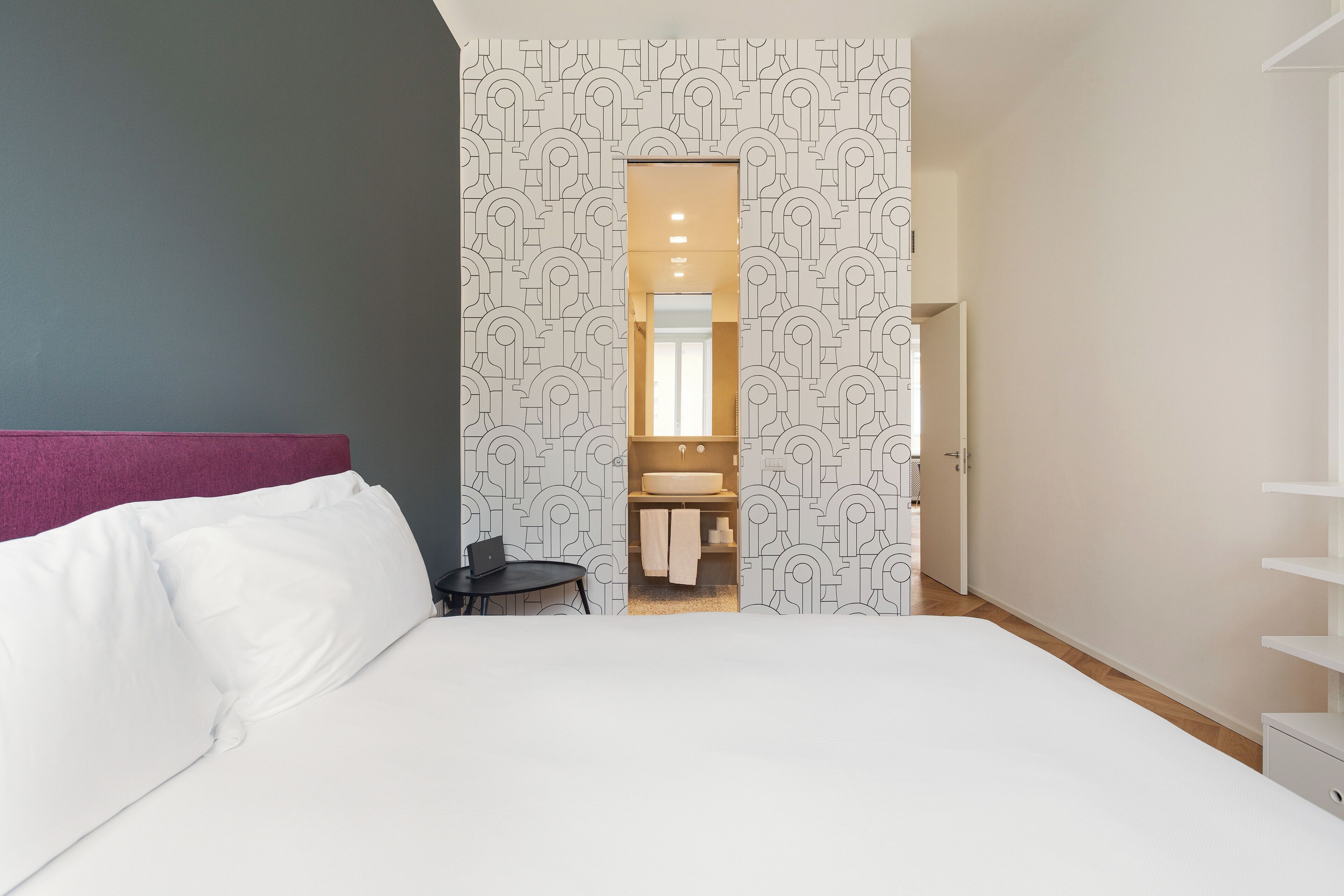 Un dormitorio moderno con una cama grande, un escritorio pequeño y un baño visible a través de una puerta.