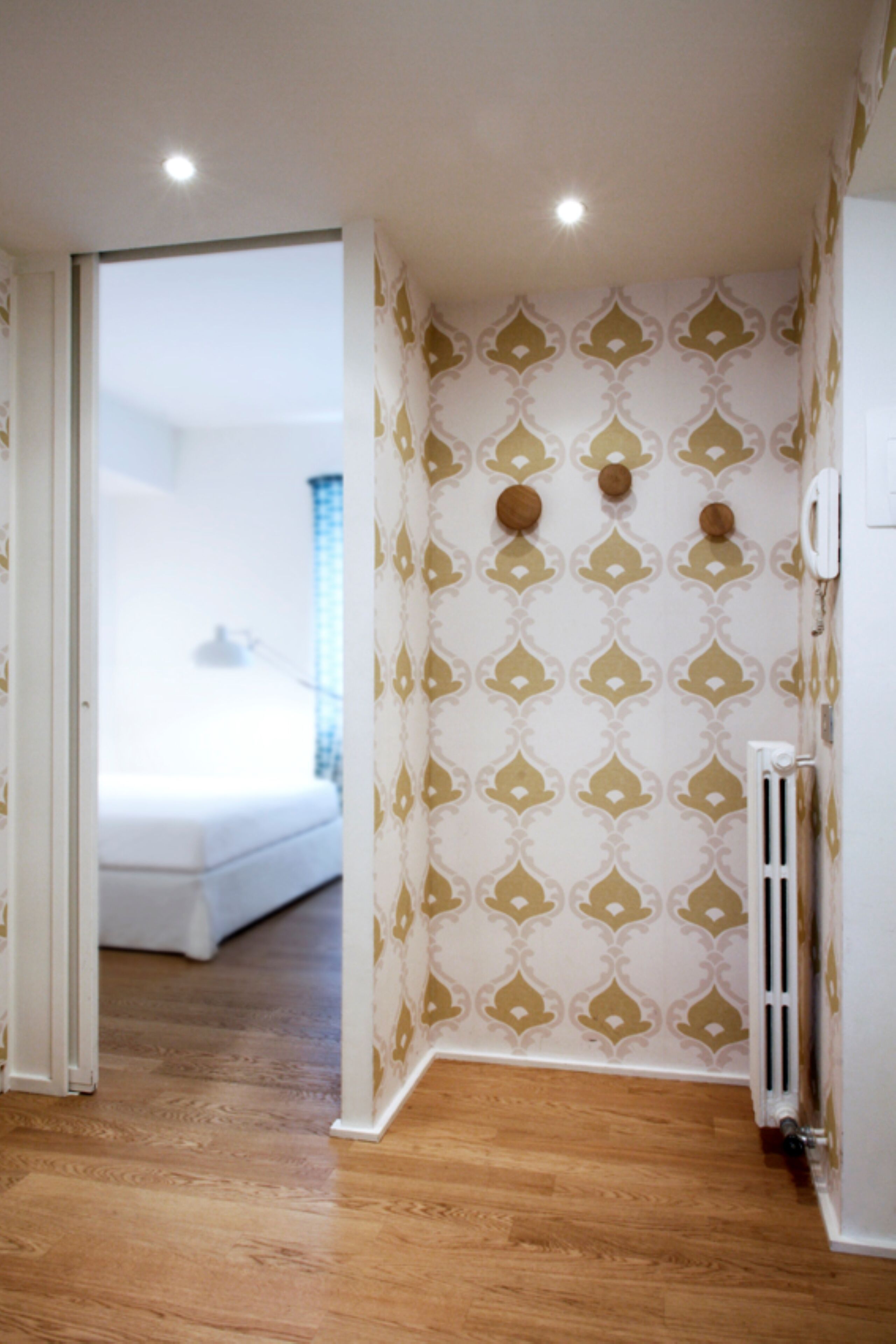 A hotel room with a patterned wallpaper, wooden flooring, a radiator, and a bed in the background.