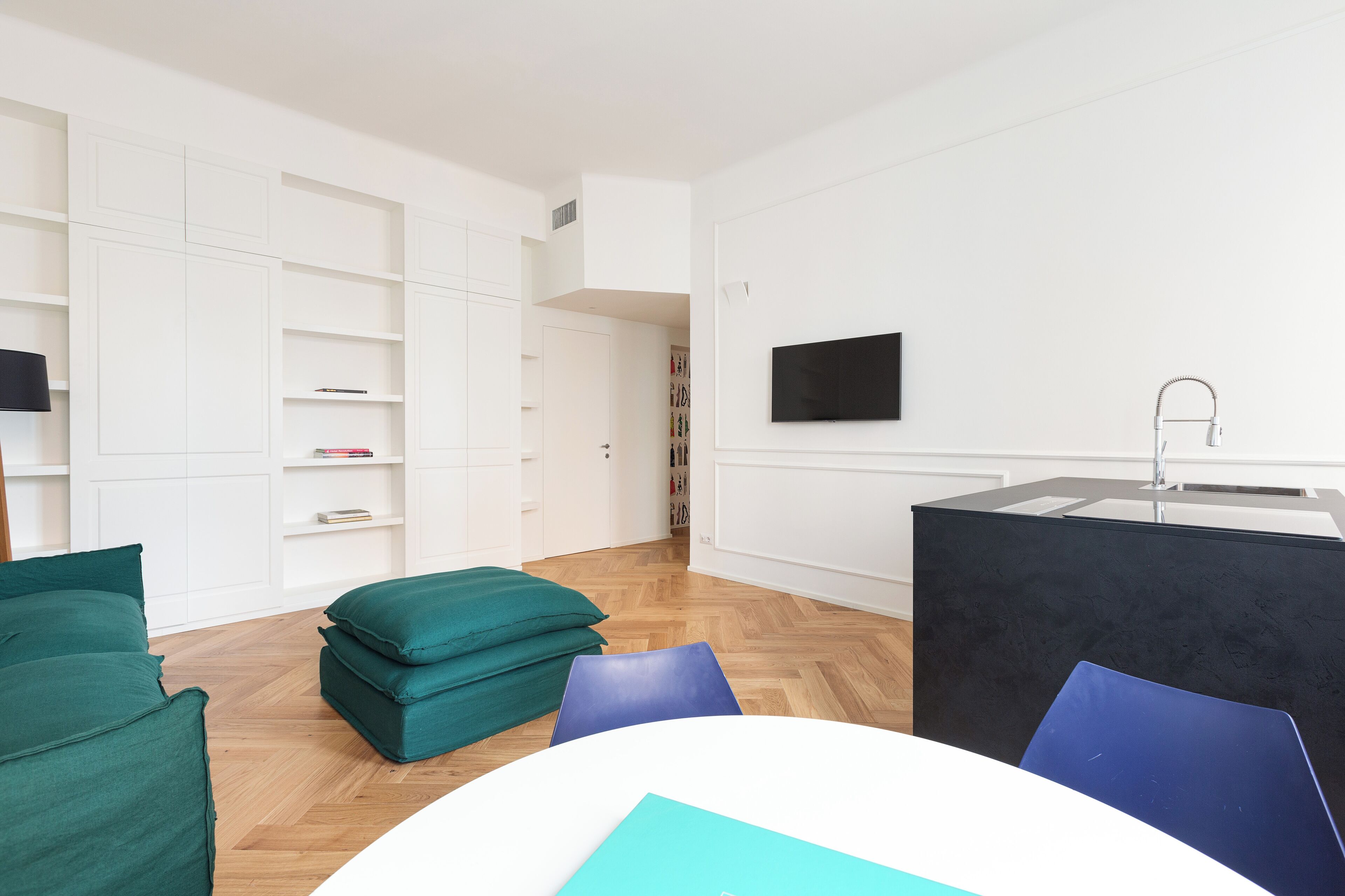 A modern, minimalist living room with a white sofa, teal cushions, a blue chair, and a black coffee table.