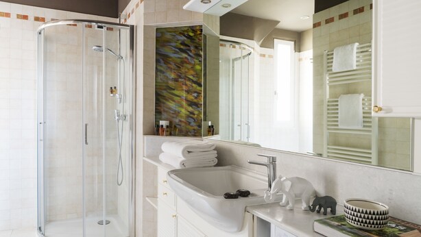 A modern bathroom with a glass-enclosed shower, a large mirror, and a vanity with a sink and decorative items. - Brera Apartments in San Fermo (Milan)