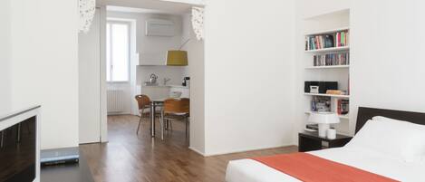 A hotel room with a bed, a TV, a bookshelf, a desk, and a dining area.