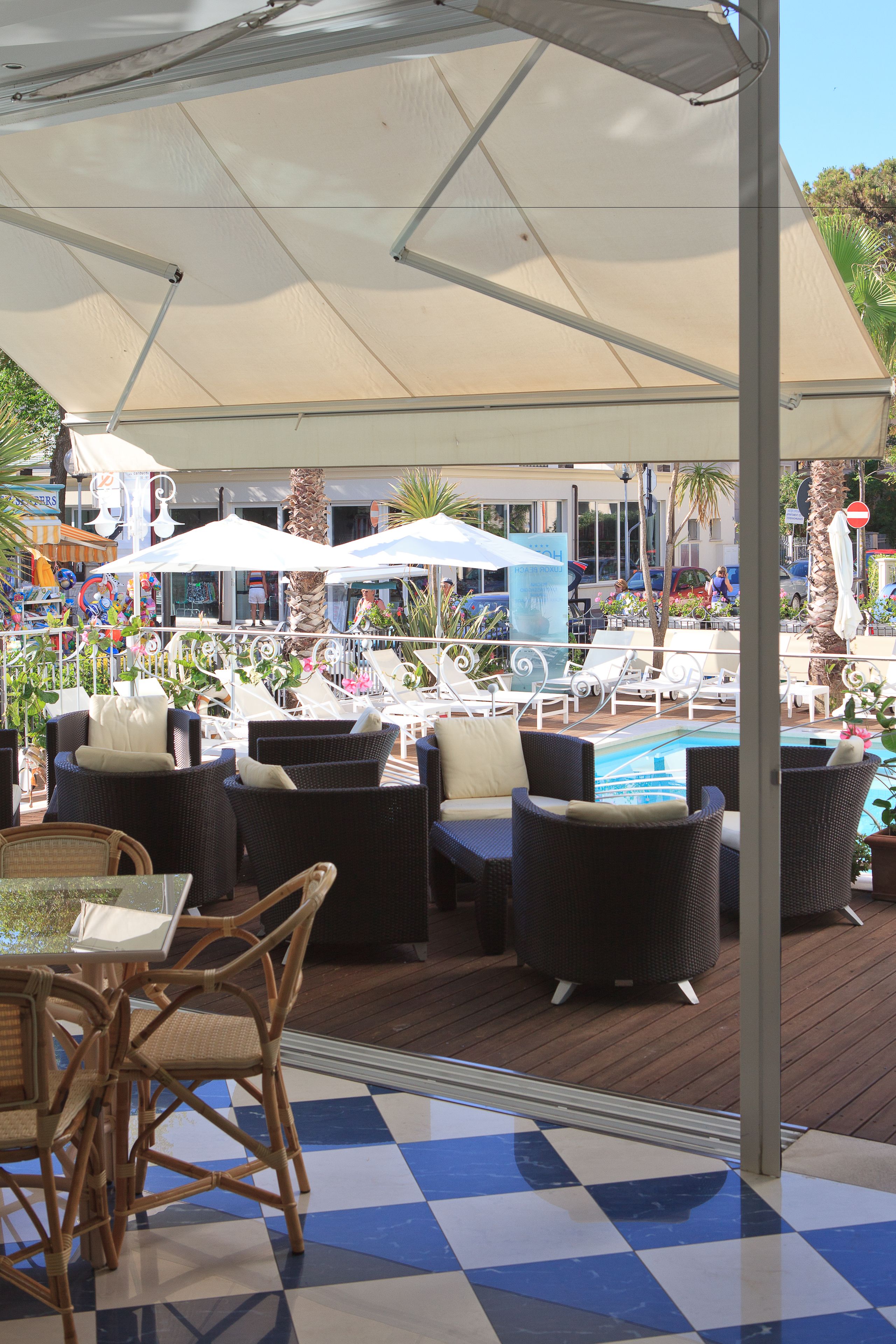 A poolside area with lounge chairs and umbrellas, a pool, and a checkered floor.