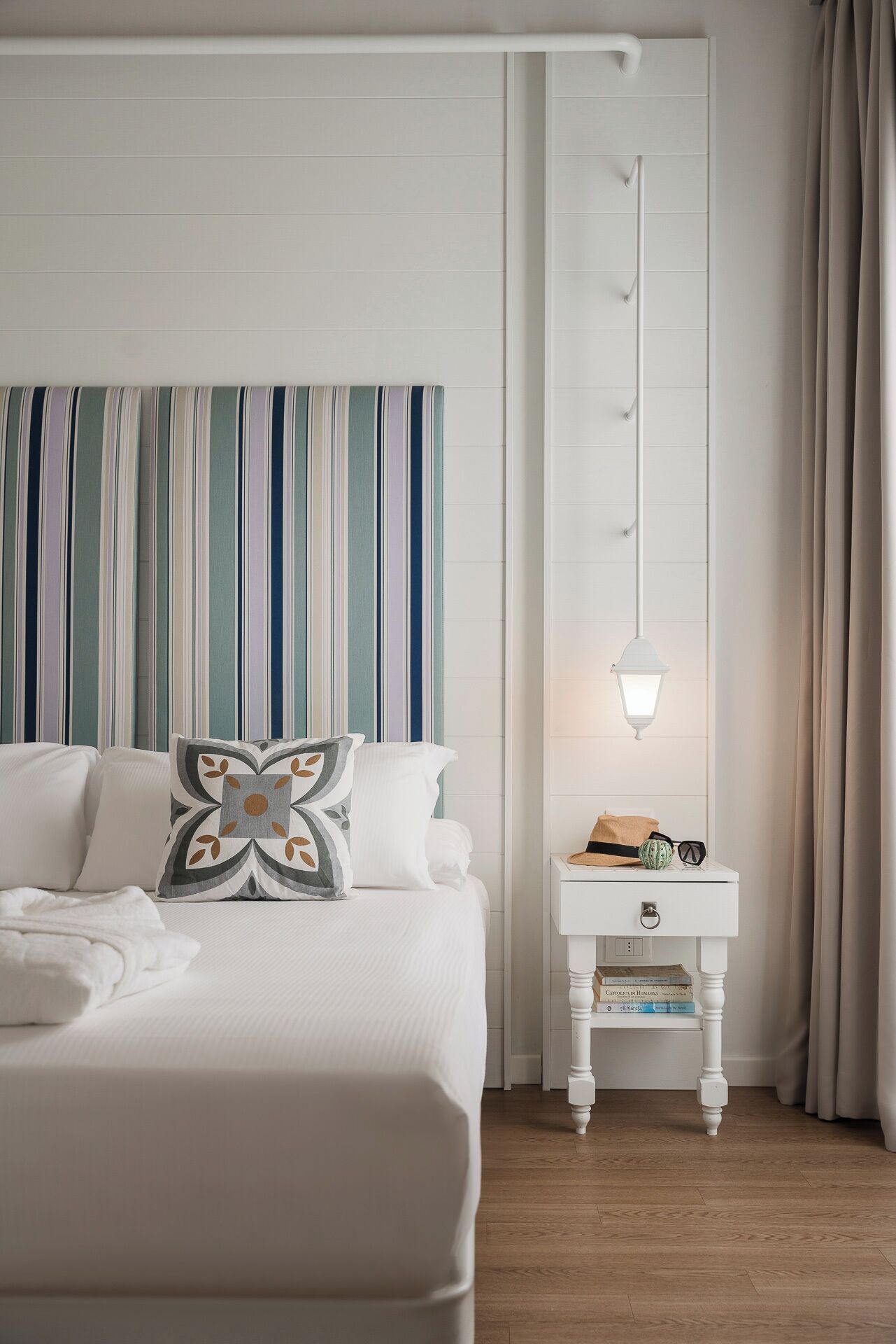 A neatly arranged hotel room with a bed, a bedside table with a lamp, and a striped curtain.