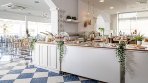Een moderne hotel lobby met een geruit vloertapijt, een centraal gelegen bar met eten en drinken, en een zithoek met stoelen en tafels.