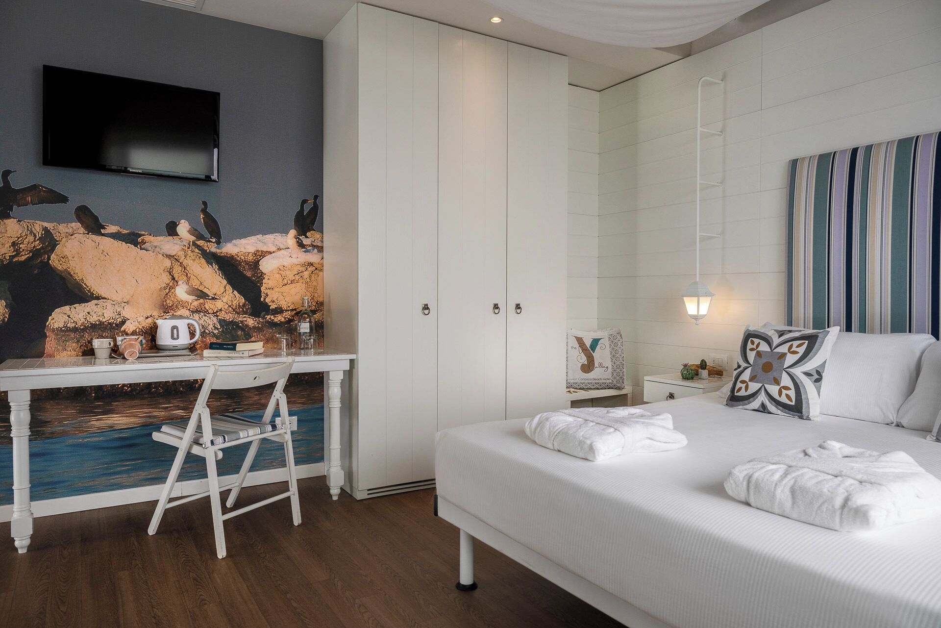 A hotel room with a bed, a desk with a chair, a television, and a wall with a mural.