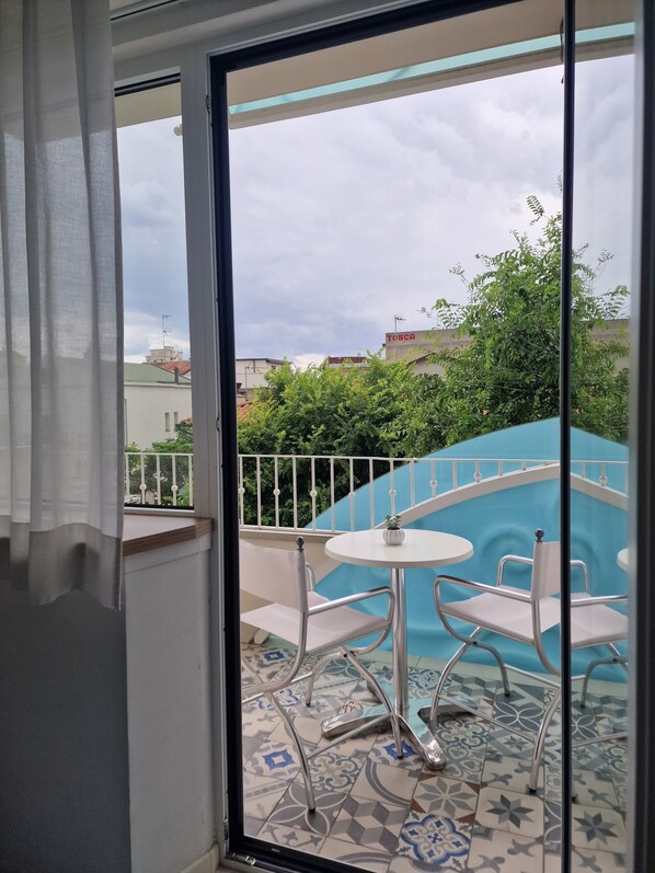 Un balcón con pared azul, sillas blancas y una pequeña mesa.