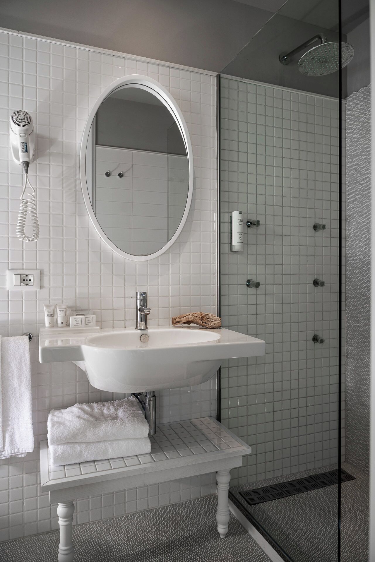 A bathroom with a white sink, a round mirror, a hairdryer, and a shower area.