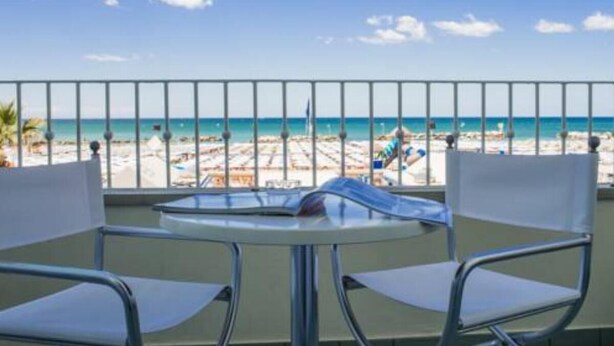 Een balkon met uitzicht op een strand, een ronde tafel en twee witte stoelen.