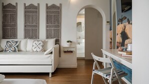 Een moderne kamer met een witte bank, een klein tafeltje met boeken en een plant, en een schilderij van vogels aan de muur.