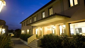 A two-story building with a covered entrance, steps leading up to the main door, and a well-lit facade. - Hotel Alba Roma (Rome)