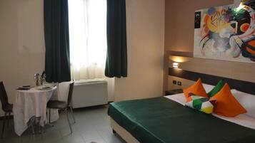 A hotel room with a bed, a dining table with chairs, a radiator, and a painting on the wall.