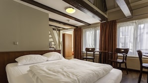Ein Hotelzimmer mit einem großen Bett, einem Holz-Kopfteil, einem Schreibtisch mit zwei Stühlen und einem Fenster mit Vorhängen.