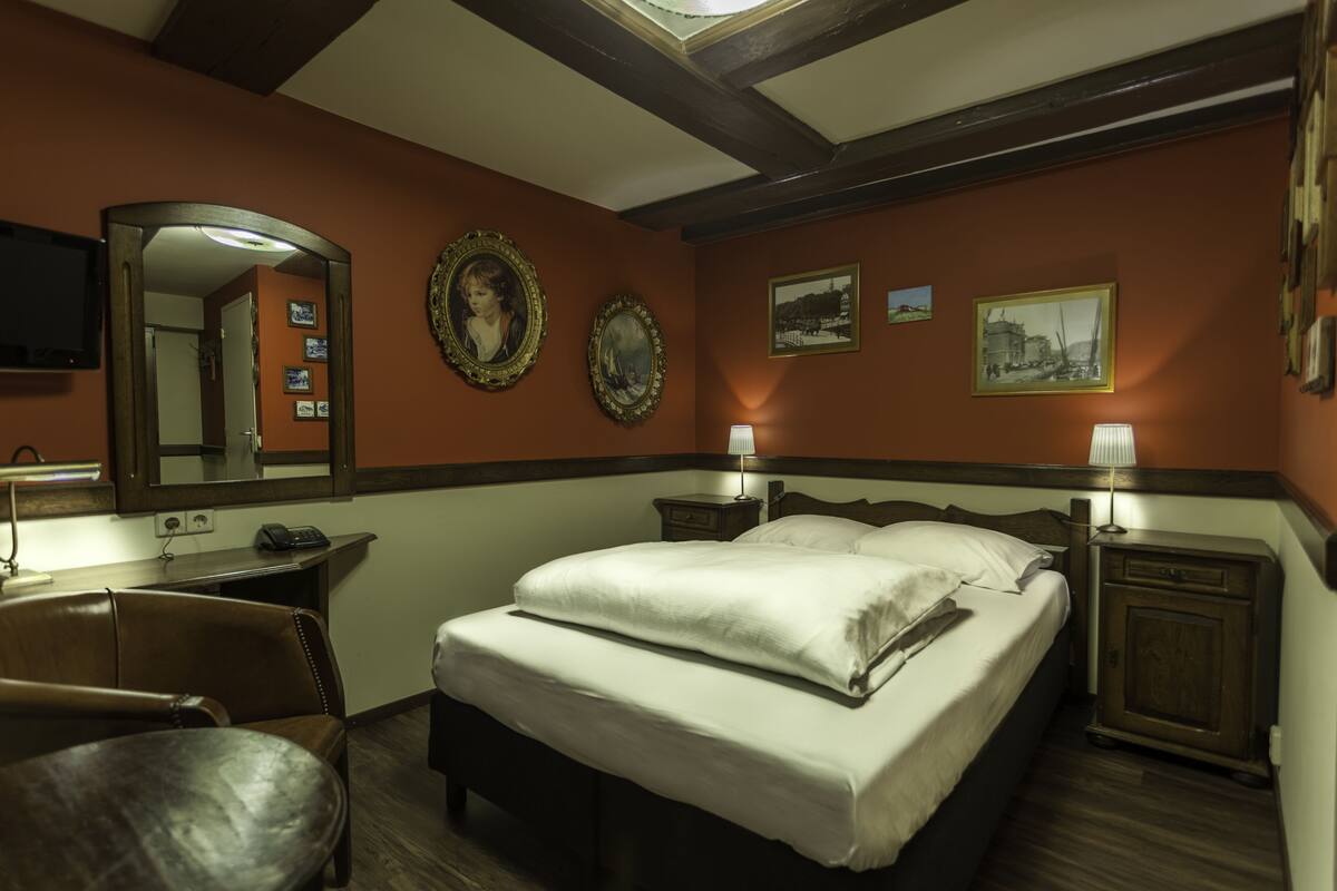 Quarto de hotel com uma cama grande, duas mesas de cabeceira, uma escrivaninha, uma cadeira e um espelho.