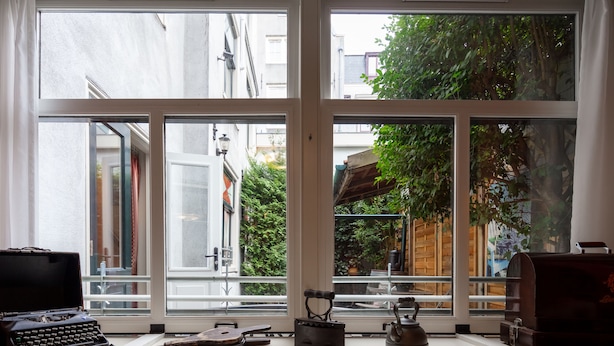 Ein Zimmer mit großem Fenster und Blick auf einen Garten sowie Gebäude.